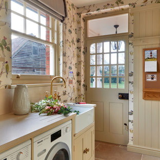Ispirazione per una lavanderia multiuso tradizionale di medie dimensioni con lavello stile country, ante con riquadro incassato, ante beige, top in quarzo composito, paraspruzzi beige, paraspruzzi in quarzo composito, pareti beige, pavimento in pietra calcarea, lavatrice e asciugatrice affiancate, pavimento beige, top beige e carta da parati