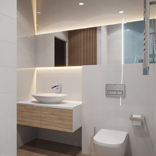 Diseño de cuarto de baño contemporáneo, pequeño, con armarios con paneles lisos, sanitario de pared, baldosas y/o azulejos blancos, baldosas y/o azulejos de cerámica, paredes blancas, suelo de baldosas de porcelana, encimera de acrílico, suelo marrón, encimeras blancas, puertas de armario de madera clara y lavabo sobreencimera