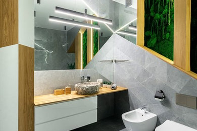 На фото: ванная комната в современном стиле с фасадами цвета дерева среднего тона, гидромассажной ванной, серой плиткой, серыми стенами, полом из керамической плитки, столешницей из дерева, серым полом и желтой столешницей
