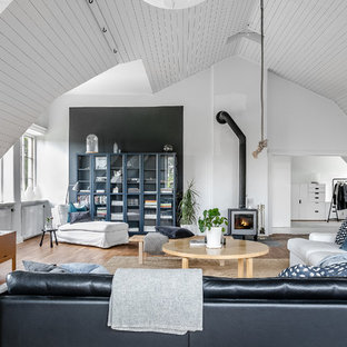 Foto på ett skandinaviskt allrum med öppen planlösning, med vita väggar, ljust trägolv, en öppen vedspis, en spiselkrans i metall och en fristående TV