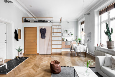 На фото: маленькая открытая гостиная комната в скандинавском стиле с белыми стенами и паркетным полом среднего тона для на участке и в саду с