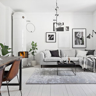 Skandinavisches Wohnzimmer mit weißer Wandfarbe, gebeiztem Holzboden, Eckkamin, gefliester Kaminumrandung und weißem Boden in Stockholm