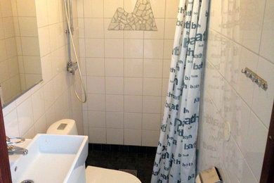 Foto på ett litet funkis badrum med dusch, med möbel-liknande, vita skåp, en öppen dusch, en vägghängd toalettstol, vit kakel, cementkakel, vita väggar, cementgolv och ett väggmonterat handfat