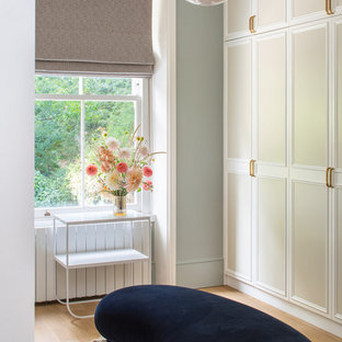Inspiration for a classic walk-in wardrobe for women in London with recessed-panel cabinets, beige cabinets, medium hardwood flooring and brown floors.
