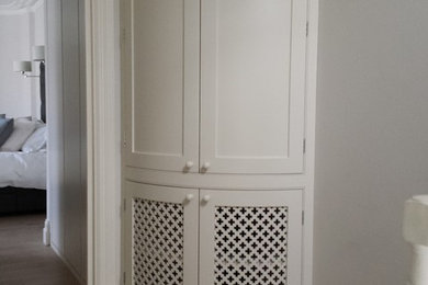 Inspiration for a small traditional wardrobe in London with shaker cabinets, white cabinets and medium hardwood flooring.