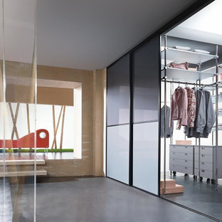 Foto di una grande cabina armadio unisex design con ante di vetro, ante grigie e pavimento in cemento