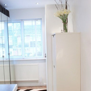 Foto di una cabina armadio unisex minimal di medie dimensioni con pavimento in compensato, ante lisce e ante bianche