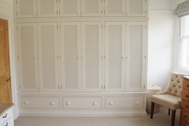 Inspiration for a medium sized classic gender neutral standard wardrobe in Sussex with recessed-panel cabinets, white cabinets, carpet and beige floors.