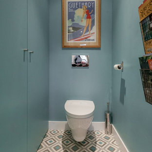 Réalisation d'un WC et toilettes design de taille moyenne avec des portes de placard bleues, un WC suspendu, un mur bleu et un sol en carrelage de céramique.