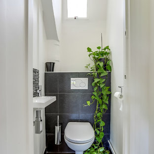 Inspiration pour un WC et toilettes design de taille moyenne avec un lavabo suspendu, un WC suspendu, un carrelage noir et un mur blanc.