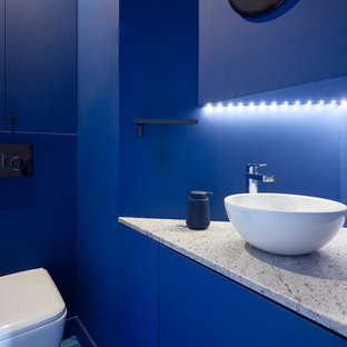 Idée de décoration pour un WC et toilettes design avec un placard à porte plane, des portes de placard bleues, un WC suspendu, un mur bleu, une vasque, un sol bleu et un plan de toilette gris.