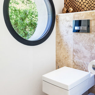 Idée de décoration pour un WC et toilettes design de taille moyenne avec un WC suspendu, un carrelage de pierre, un mur blanc et un sol beige.