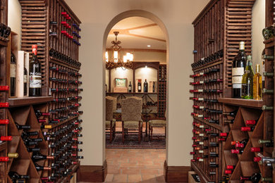 Huge tuscan terra-cotta tile and red floor wine cellar photo in Los Angeles with storage racks