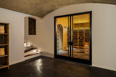 This is an example of a large rustic wine cellar in Surrey with concrete flooring and storage racks.