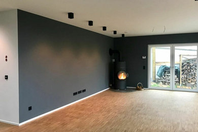 Offenes Modernes Wohnzimmer mit grauer Wandfarbe, dunklem Holzboden, Kaminofen und braunem Boden in Hamburg