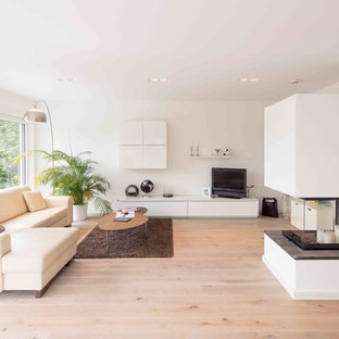 Mittelgroßes Modernes Wohnzimmer mit weißer Wandfarbe, hellem Holzboden, Kaminofen, verputzter Kaminumrandung, freistehendem TV und braunem Boden in Sonstige