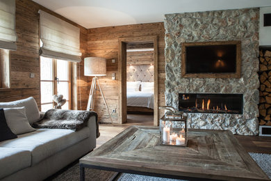 Example of a mid-sized mountain style enclosed medium tone wood floor and brown floor family room design in Munich with brown walls, a two-sided fireplace, a stone fireplace and a wall-mounted tv