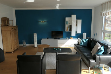 Großes, Offenes Modernes Wohnzimmer mit blauer Wandfarbe, hellem Holzboden, Kaminofen, gefliester Kaminumrandung und freistehendem TV in Frankfurt am Main