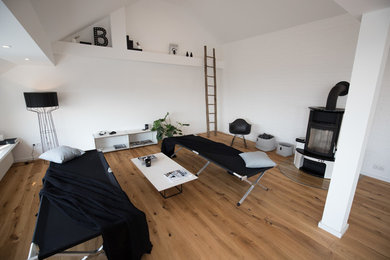 Modelo de salón abierto contemporáneo de tamaño medio sin televisor con paredes blancas, suelo de madera en tonos medios, estufa de leña y suelo marrón