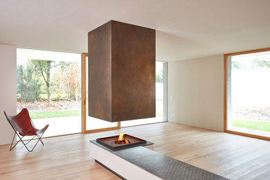 Foto de sala de estar abierta actual grande con paredes blancas, suelo de madera clara, chimenea de doble cara, marco de chimenea de metal y suelo beige
