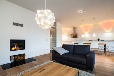 Offenes Modernes Wohnzimmer mit weißer Wandfarbe, braunem Holzboden, Kamin und verputzter Kaminumrandung in Köln