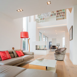Großes, Offenes, Repräsentatives Modernes Wohnzimmer mit weißer Wandfarbe, braunem Holzboden, Gaskamin, verputzter Kaminumrandung, Multimediawand und beigem Boden in Düsseldorf