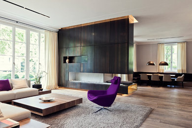 Großes, Offenes Modernes Wohnzimmer mit braunem Holzboden, Hängekamin, Kaminumrandung aus Metall, verstecktem TV und beiger Wandfarbe in Essen
