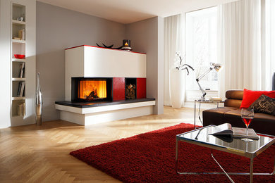 Diseño de salón actual con paredes grises, suelo de madera clara, chimenea de doble cara y marco de chimenea de yeso