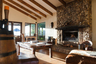 Ejemplo de sala de estar abierta rural grande con paredes beige, suelo de madera en tonos medios, todas las chimeneas, marco de chimenea de piedra y suelo marrón