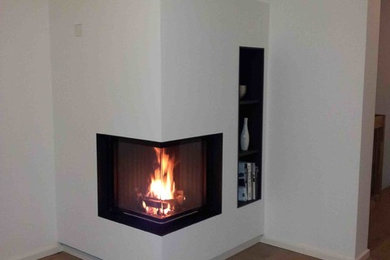ケルンにある低価格の中くらいなモダンスタイルのおしゃれなLDK (白い壁、無垢フローリング、コーナー設置型暖炉、漆喰の暖炉まわり、茶色い床) の写真