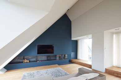 Modelo de sala de juegos en casa abierta contemporánea grande con paredes azules, suelo de madera clara, estufa de leña, televisor colgado en la pared y suelo beige
