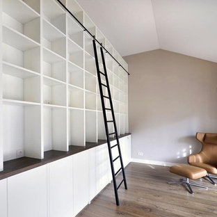 Abgetrennte, Geräumige, Fernseherlose Moderne Bibliothek mit brauner Wandfarbe, braunem Holzboden, Kamin, verputzter Kaminumrandung und braunem Boden in München
