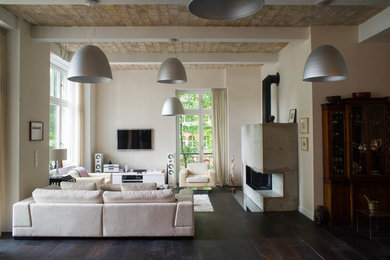Modelo de sala de estar actual con paredes blancas, suelo de madera oscura, chimenea de esquina, marco de chimenea de hormigón y televisor colgado en la pared