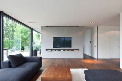 Cette image montre une salle de séjour design ouverte avec un mur gris, un sol en bois brun et un téléviseur encastré.