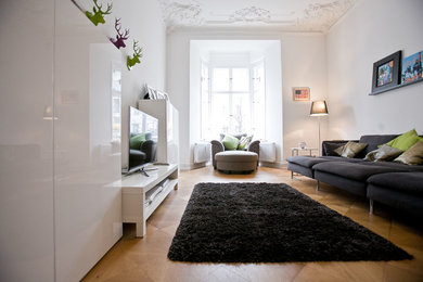 Großes, Abgetrenntes Modernes Wohnzimmer ohne Kamin mit weißer Wandfarbe, braunem Holzboden und freistehendem TV in Berlin