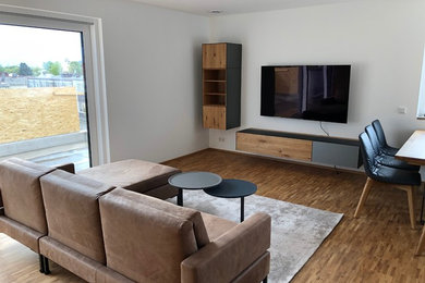 Mittelgroßes, Offenes Modernes Wohnzimmer mit weißer Wandfarbe, braunem Holzboden und TV-Wand in Nürnberg
