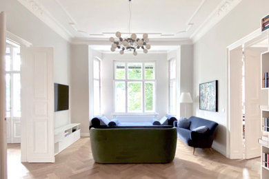 Imagen de sala de estar con biblioteca abierta actual grande sin chimenea con paredes grises, suelo de madera clara y televisor colgado en la pared