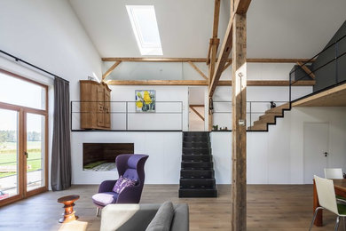 Modelo de salón abierto campestre de tamaño medio con paredes blancas, suelo de madera en tonos medios y suelo marrón