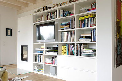 Große, Offene Moderne Bibliothek mit weißer Wandfarbe, braunem Holzboden, freistehendem TV und braunem Boden in Sonstige