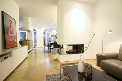Ejemplo de sala de estar abierta contemporánea de tamaño medio con paredes blancas, suelo de madera clara, todas las chimeneas, marco de chimenea de yeso y televisor colgado en la pared
