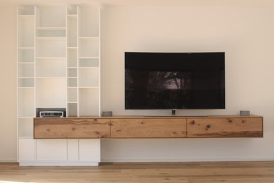 Diseño de salón abierto moderno de tamaño medio con paredes blancas, suelo de madera en tonos medios, pared multimedia y suelo marrón