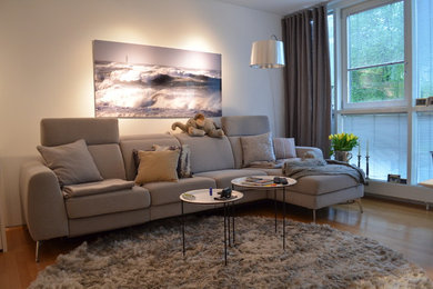 Modelo de salón abierto nórdico pequeño con paredes blancas, suelo de madera en tonos medios y televisor colgado en la pared