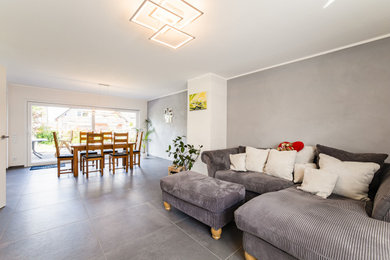 Geräumiges, Offenes Modernes Wohnzimmer mit weißer Wandfarbe, Kaminofen, freistehendem TV und grauem Boden in Düsseldorf