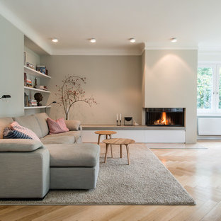 Ejemplo de salón abierto, nórdico, grande, con paredes beige, suelo de madera clara, chimenea lineal y marco de chimenea de yeso