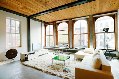 Großes, Offenes Industrial Wohnzimmer ohne Kamin mit weißer Wandfarbe, Betonboden und freistehendem TV in Berlin