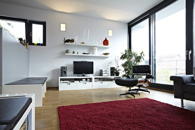 Ejemplo de salón abierto actual de tamaño medio sin chimenea con paredes blancas, suelo de madera clara y pared multimedia