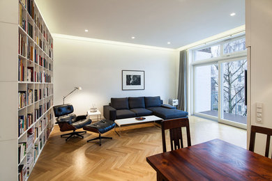 Ejemplo de sala de estar con biblioteca abierta actual de tamaño medio sin chimenea con paredes blancas, suelo de madera en tonos medios y suelo marrón