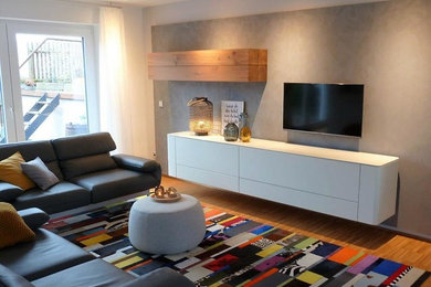 Ejemplo de sala de estar abierta contemporánea de tamaño medio con paredes grises, suelo de madera clara, todas las chimeneas, televisor colgado en la pared y suelo marrón