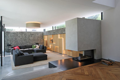 This is an example of a large contemporary mezzanine games room in Munich with grey walls, concrete flooring, a concrete fireplace surround, a concealed tv, grey floors and a two-sided fireplace.