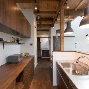 This is an example of a mid-sized asian galley eat-in kitchen in Sapporo with dark wood cabinets, stainless steel benchtops, dark hardwood floors, flat-panel cabinets, a peninsula, an integrated sink, white splashback and black appliances.